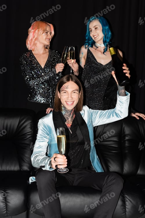 Preview: tattooed queer man with bottle of champagne near nonbinary friends clinking glasses on black