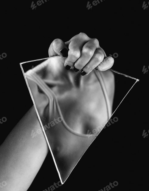 Preview: Female adult holding a handheld mirror in her left hand that reflects her chest in grayscale