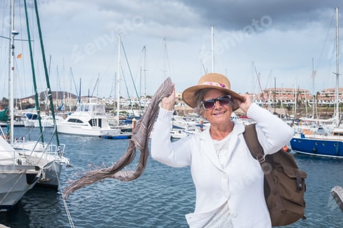 Preview: Smiling senior woman enjoying sea excursion at harbour in a windy summer day