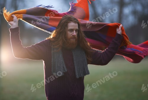 Preview: Man wrapping blanket around himself in countryside