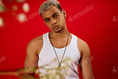 Preview: Stylish young man posing confidently in red studio with trendy fashion choices