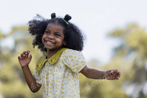 Preview: African black child with curly hair is jumping happily in the water spray at outdoor