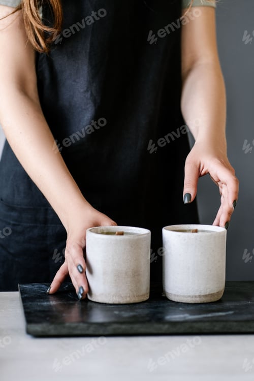Preview: Hands Arranging Scented Candles on a Black Surface