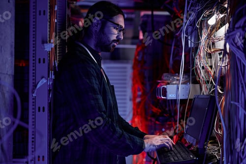 Preview: Bearded system administrator setting up server network in neon light