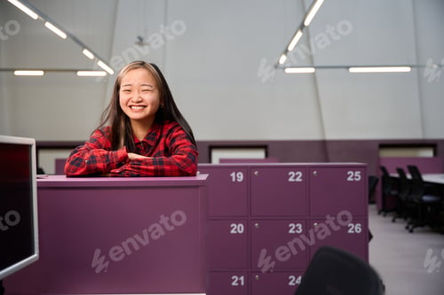 Preview: Young laughing asian female IT employee looking at camera standing by cupboard