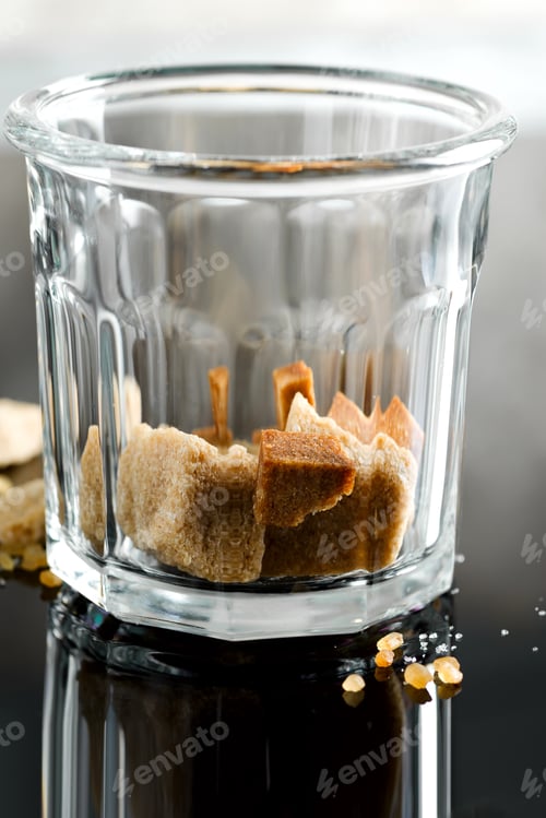 Preview: Close up glass with brown cane cubes on a dark background with reflection