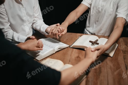 Preview: Group of Christians sit together and pray around a wooden table with blurred open Bible pages