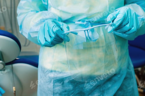 Preview: close up of a dentist's hands holding a protective plastic screen in his office