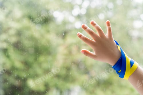 Preview: cropped view of child with blue and yellow ribbon touching windows glass with raindrops