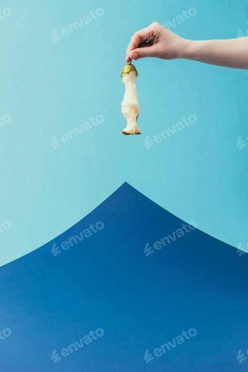 Preview: partial view of woman holding pear core in hand on blue background