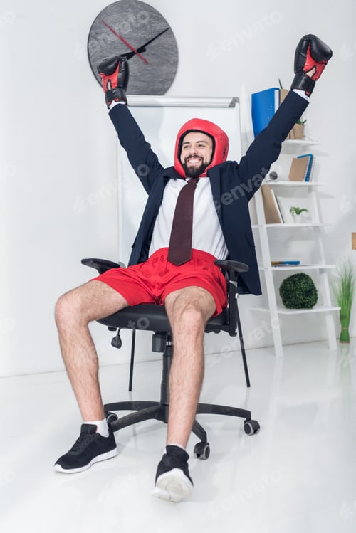 Preview: portrait of happy businessman in boxing equipment sitting on chair in office