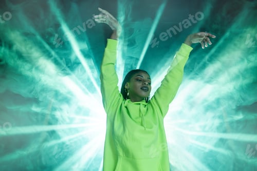 Preview: From below of young African American female in hoodie raising hands while standing against green