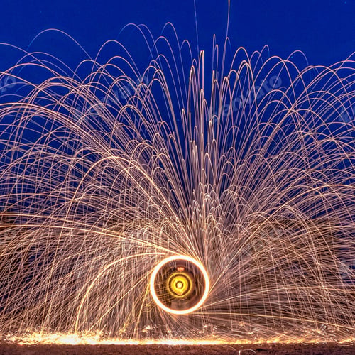 Preview: Man radiating fireworks from a center of an iron wool circle against a blue sky