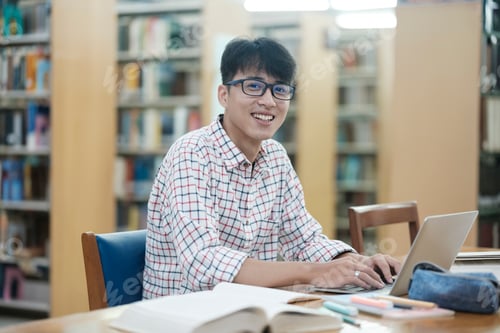 Preview: Young Asian male sitting inside a library alone doing research.
