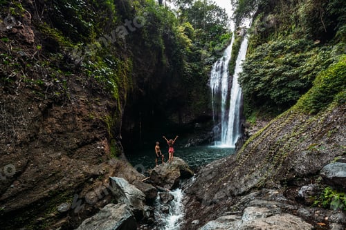 Preview: Lovers at the waterfall, rear view. Couple admiring a beautiful waterfall in Indonesia