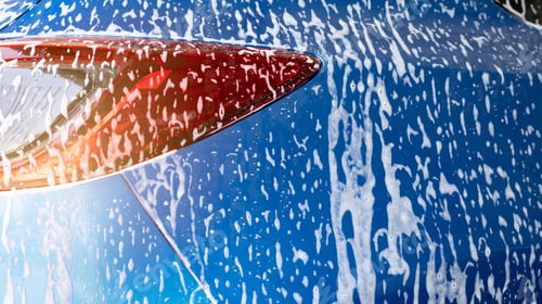 Preview: Blue car wash with white soap foam and professional auto care service. Car cleaning service concept.