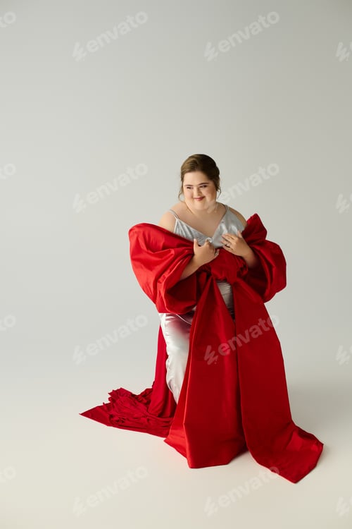 Preview: Joyful expression of a young woman with Down syndrome wrapped in red fabric at a serene studio