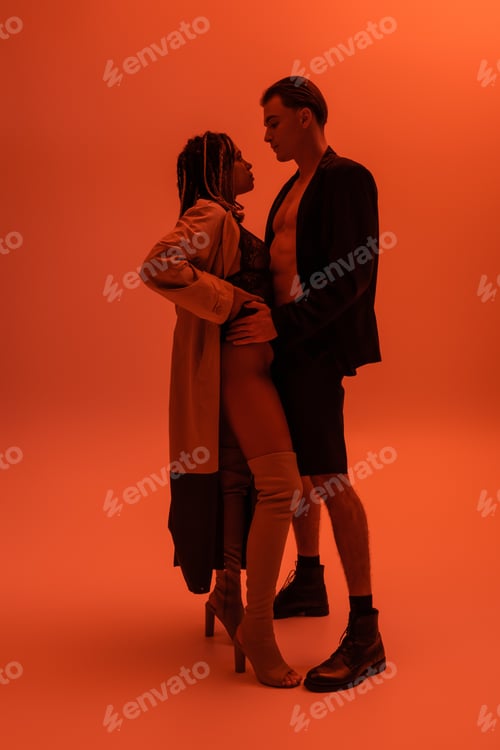 Preview: full length of man in black blazer and shorts seducing sexy african american woman in trench coat