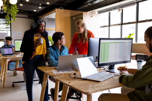 Preview: Diverse male and female colleagues in discussion using laptop at desk in office
