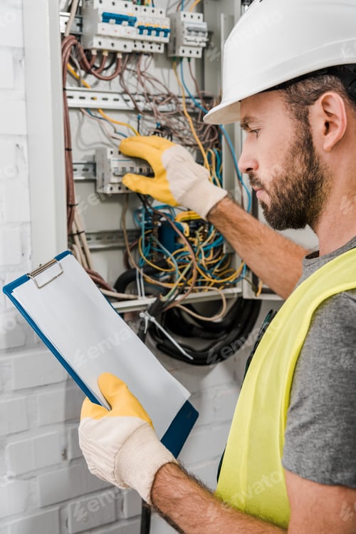 Preview: handsome electrician holding clipboard and checking electrical panel in corridor