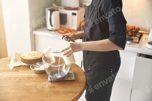 Preview: young professional female cook is preparing tasty cake at her light modern kitchen