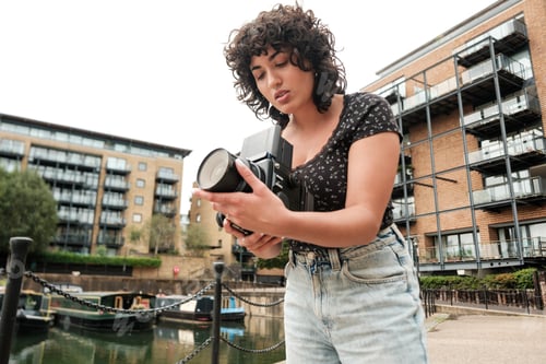 Preview: Photographer checking lens of vintage camera by canal in city