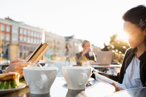 Preview: A young woman engrossed in her book at a sunny outdoor caf.