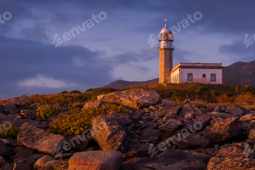 Preview: Larino Lighthouse surrounded by rocks during the sunset in Spain