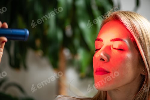 Preview: Woman wearing a red light therapy face mask during a skincare session,