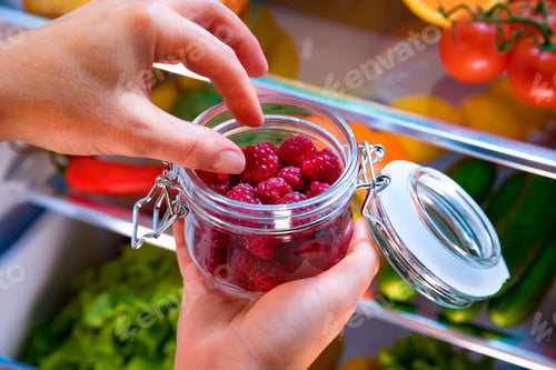 Preview: Woman takes the fresh raspberries from the open refrigerator