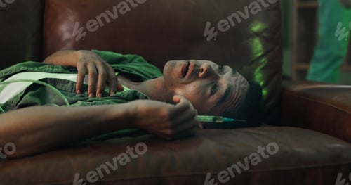 Preview: Drugs, overdose and man on sofa with needle, health risk and narcotic danger in apartment at night.