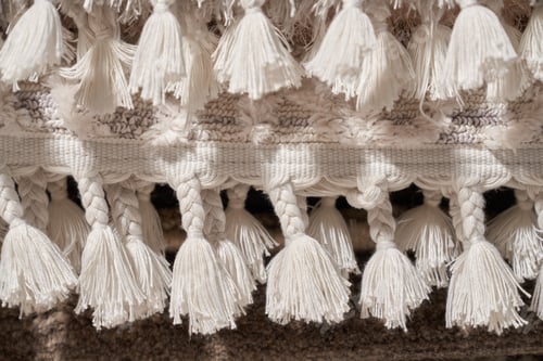 Preview: Texture of white cotton fringe on edge of beige carpet as framing.