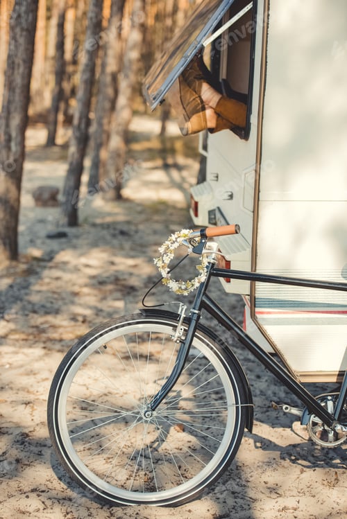 Preview: male feet sticking out of the window of trailer while bicycle with wreath standing near campervan