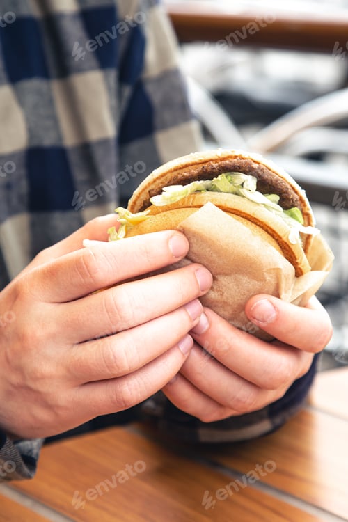 Preview: Burger in male hands close-up in a fast food cafe.