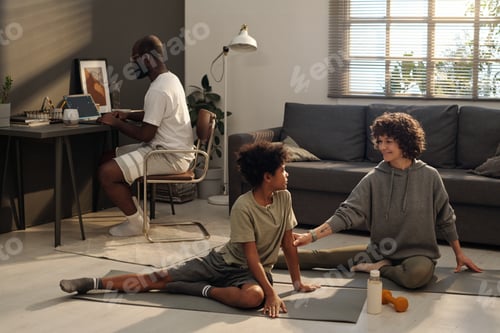 Preview: Happy woman helping her little son while both doing stretching exercise