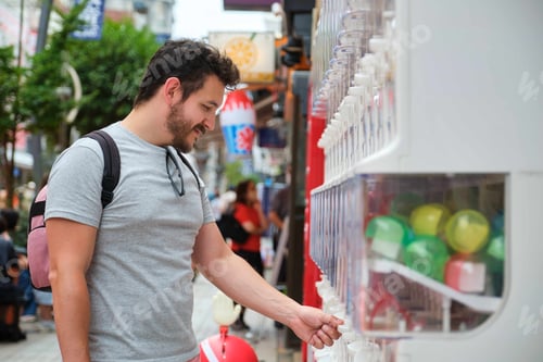 Preview: Latin tourist buying a toy capsule at gashapon machine in Tokyo.
