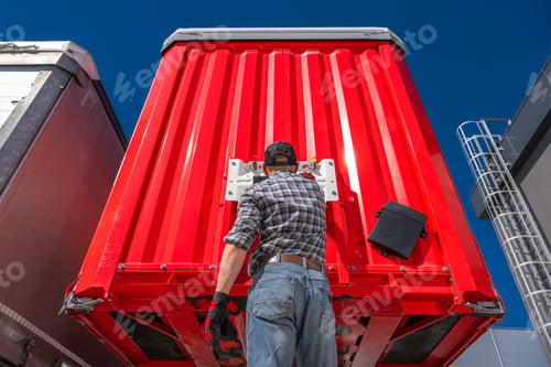 Preview: Trucker performing maintenance on the rear of a red semi trailer
