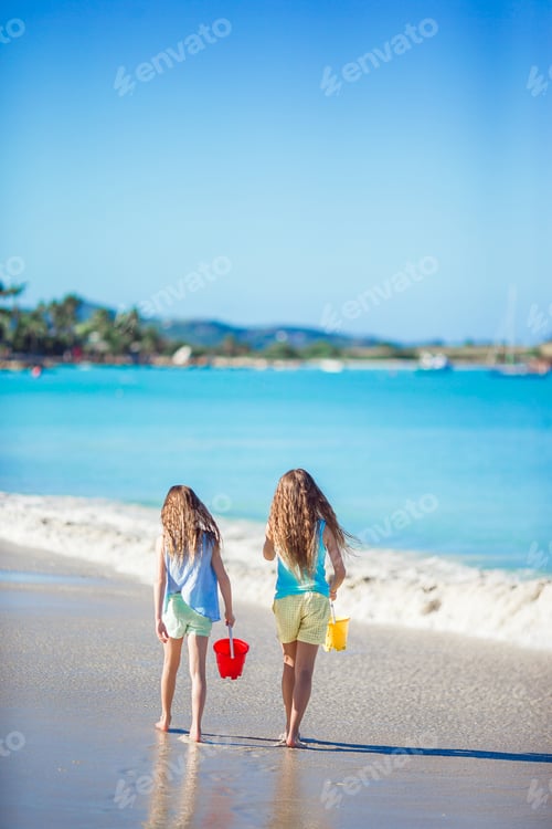 Preview: Adorable little girls playing with sand on the beach. Back view of kids walking along the beach