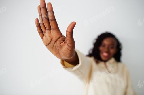 Preview: African woman in hoodie stand against white wall and show palm of the hand. Stop sign.