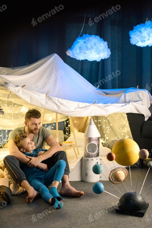 Preview: father and son sitting together in blanket fort with toy rocket and solar system model