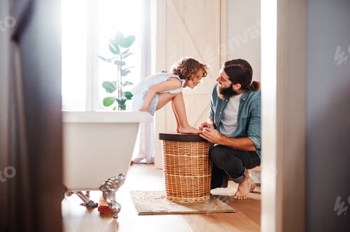 Preview: Young father painting small daugter's nails in a bathroom at home.