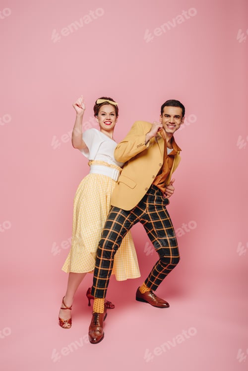 Preview: cheerful dancers looking at camera while dancing boogie-woogie on pink background