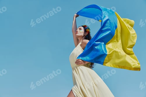 Preview: Confident Ukrainian woman carrying national flag with sky in the background