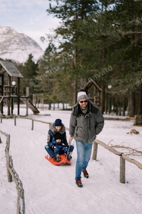 Preview: Smiling dad carries mom and little boy on a sleigh along a snowy path in the forest