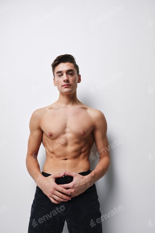 Preview: Sexy half-naked guy holds pants with his hands on a light background