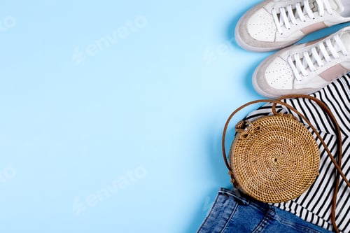 Preview: Blue jeans shorts, sneakers, striped shirt and rattan bag on blue background.