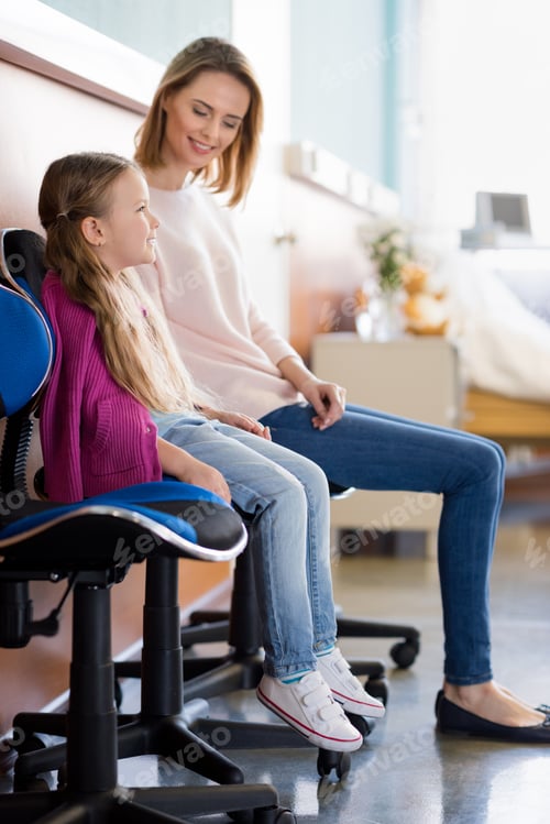 Preview: Smiling mother and daughter sitting on chairs in hospital room