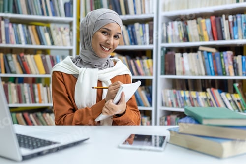 Preview: Smiling hijab-wearing student studying in library with laptop