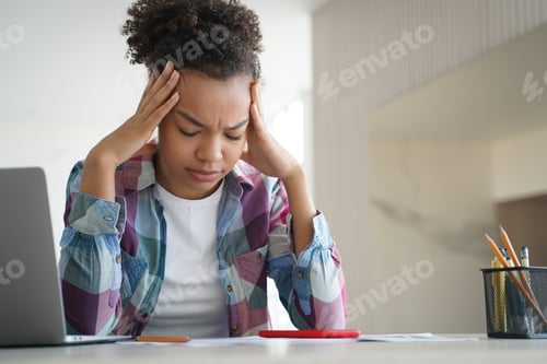Preview: Tired african american teen girl suffer headache doing homework at laptop. Difficult elearning