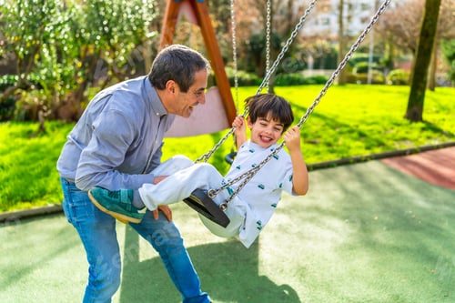 Preview: Grandfather pushing grandson on swing in playground